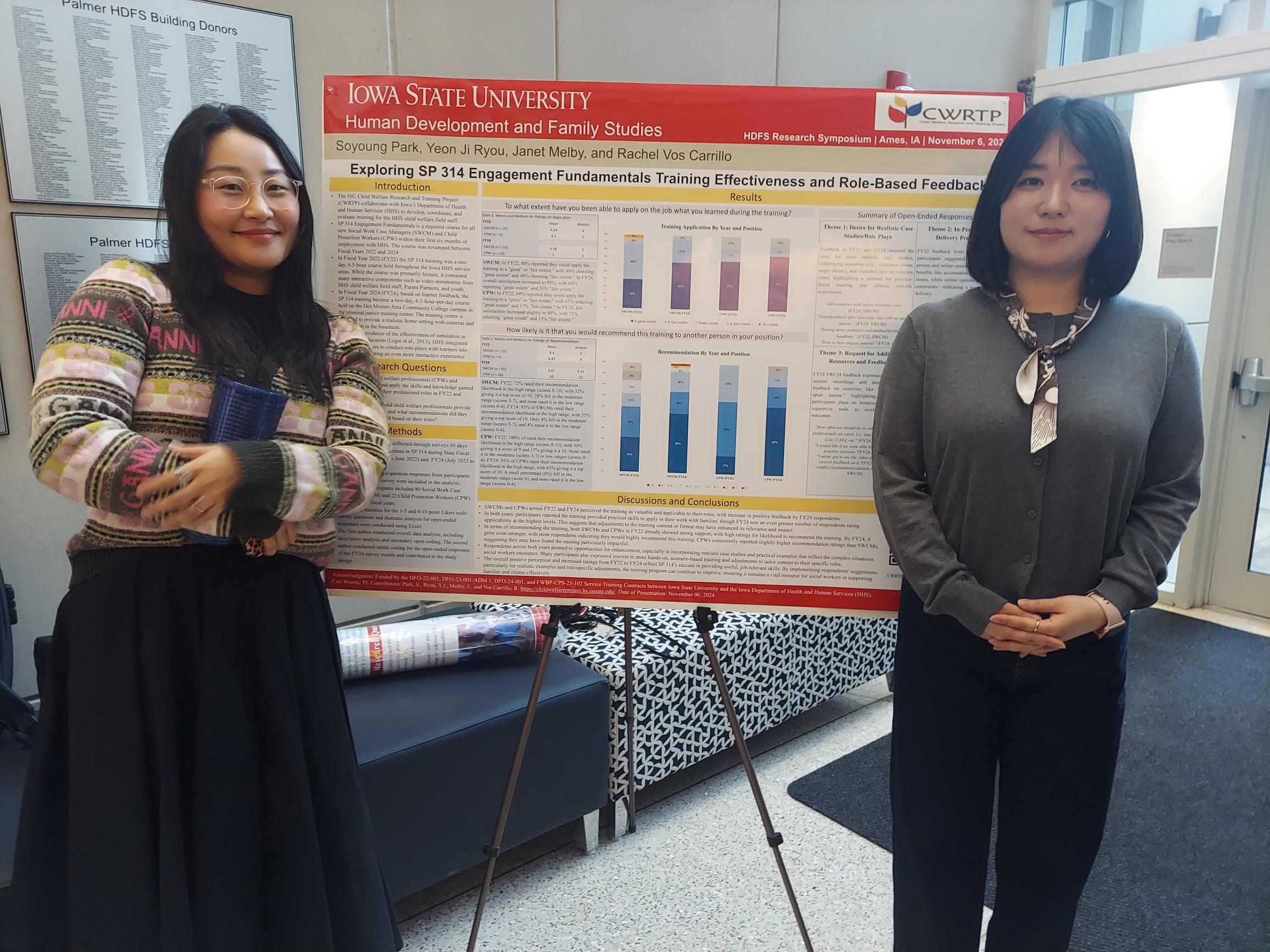 Graduate assistants Yeon Ji Ryou and Soyoung Park smile as they pose in front of their research poster, presented on an easel in a bright foyer.