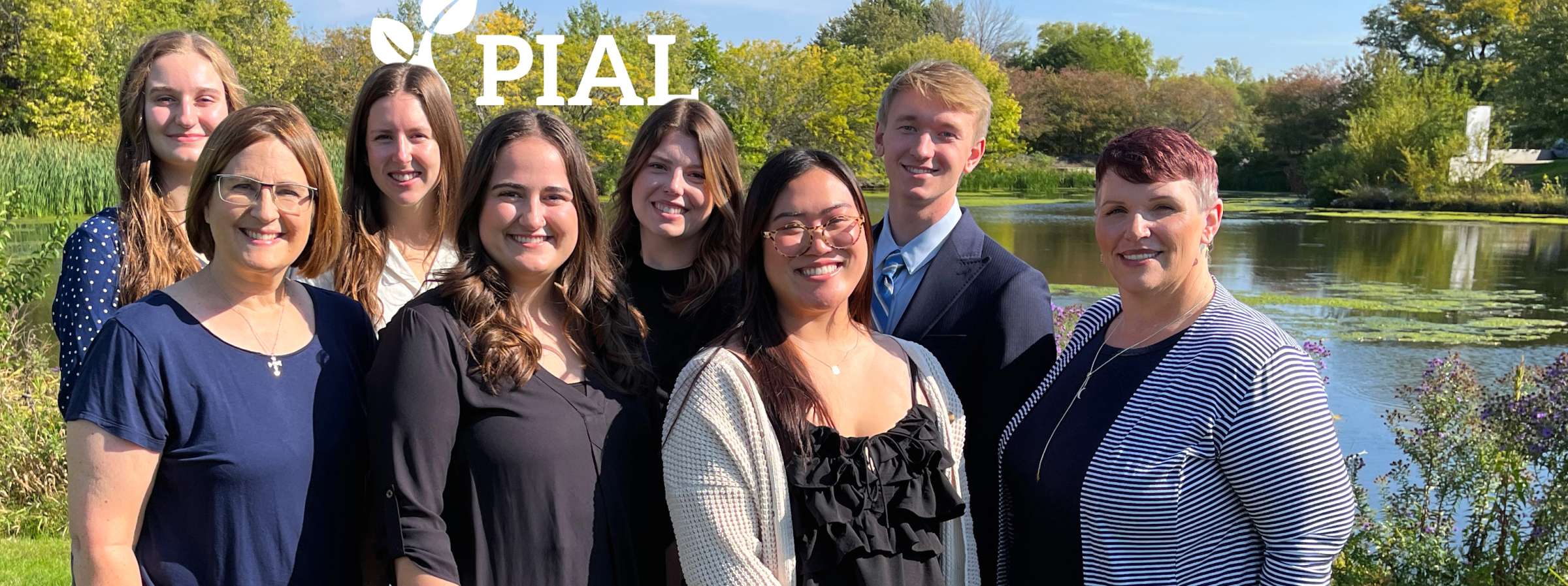 The FY24 PIAL team standing outside by a pond and smiling at the camera.