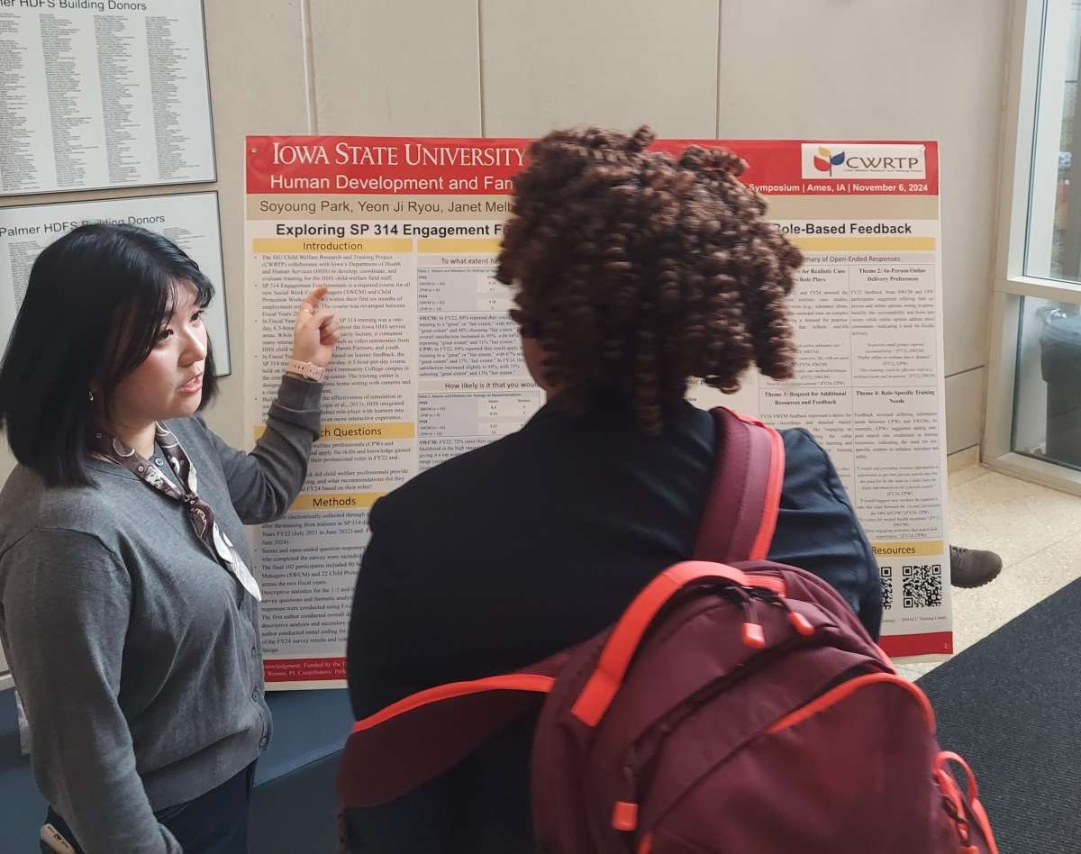 Soyoung Park pointing to her poster as she presents her poster to someone wearing a suit and carrying a red backpack