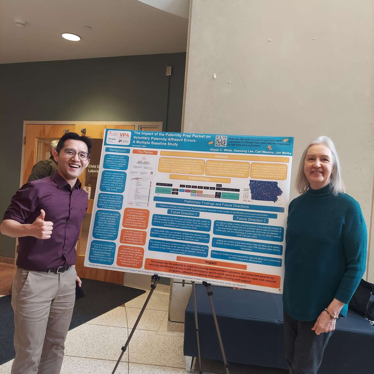 Dr. Lee and Dr. Melby stand beside Alison White's research poster in a bright foyer.