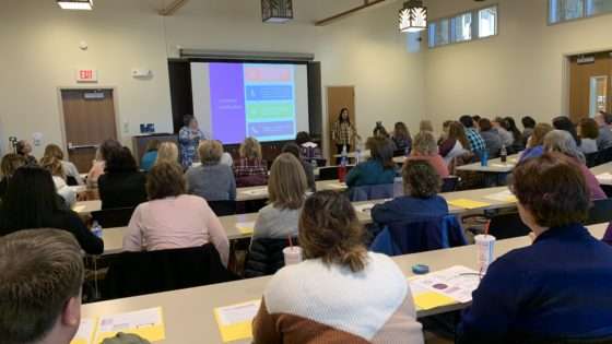 Child support employees are sitting in a large room listening to a presentation 