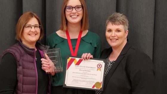 Hannah Peterson is posing with her award as Rhonda Evans and Jo Ann Lee stand beside her. They are all smiling.